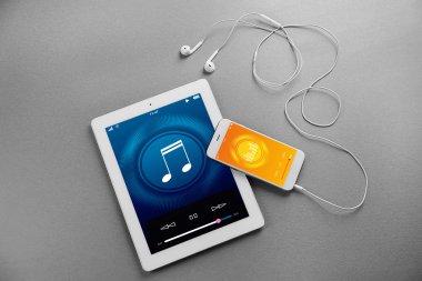 Tablet, akıllı telefon ve kulaklık gri arka plan üzerinde. Müzik çalar arayüzü ekranda.