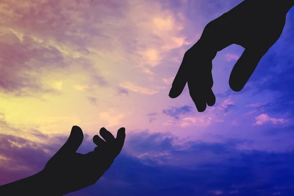 Silhuetas de pai e mãos de criança que conseguem um a outro no fundo de céu. Conceito de ajuda e cuidado . — Fotografia de Stock