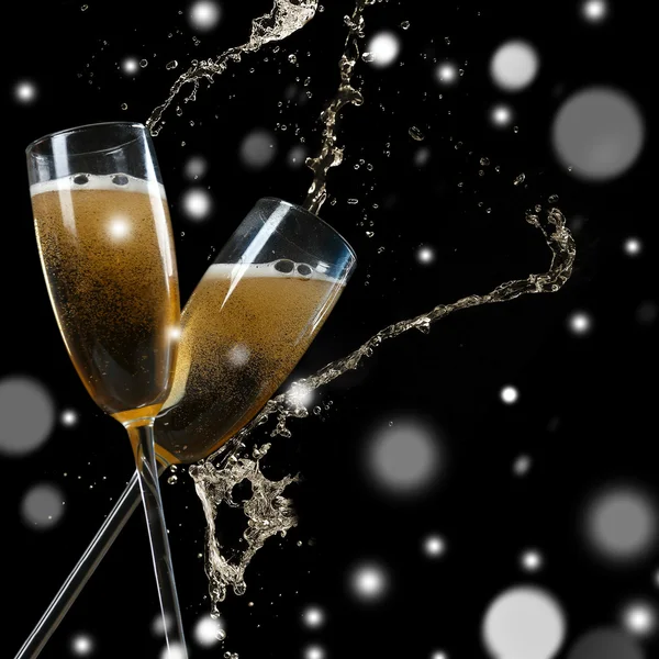 Glasses of champagne with splashes on black background. Snowy effect, Christmas celebration concept.