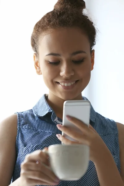 Retrato da bela menina afro-americana com café e celular — Fotografia de Stock