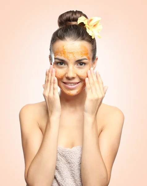 Mujer joven que aplica exfoliante en la cara contra el fondo de color. Concepto de cuidado de la piel . —  Fotos de Stock