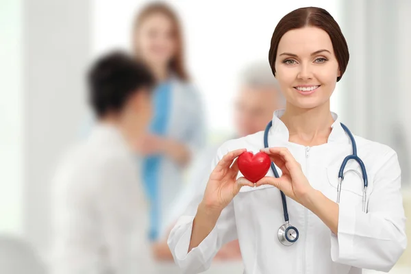 Young female doctor with red heart on blurred background. Cardiology concept.