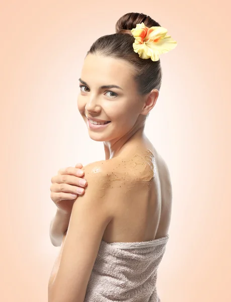 Giovane donna che applica scrub sulla spalla contro lo sfondo di colore. concetto di cura della pelle . — Foto Stock