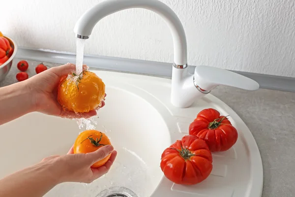 Mãos femininas lavando tomates na pia da cozinha — Fotografia de Stock