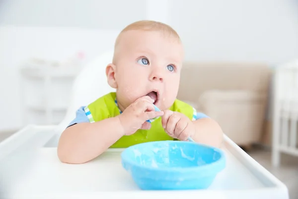 Little baby eating from bowl with spoon indoors — Stock Photo, Image