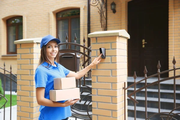 Female courier in uniform ringing in doorbell — Stock Photo, Image