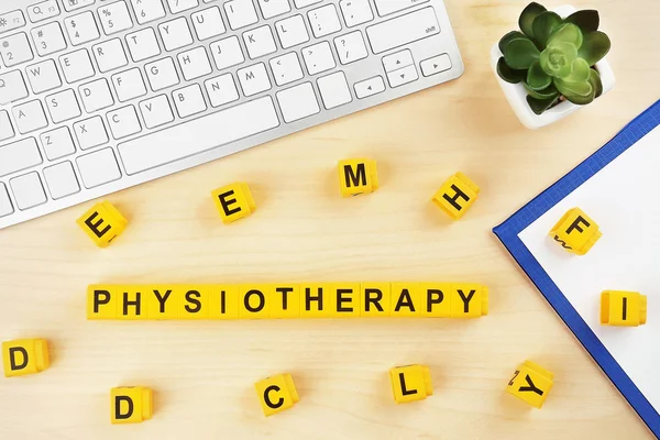 Workplace with keyboard and word PHYSIOTHERAPY made of yellow blocks on wooden background — Stock Photo, Image