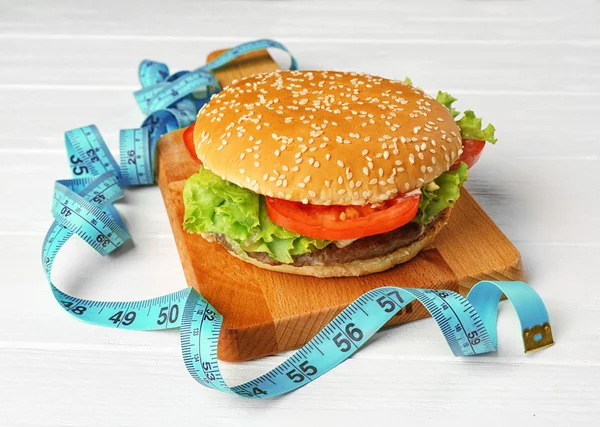 Measuring tape and tasty hamburger — Stock Photo, Image