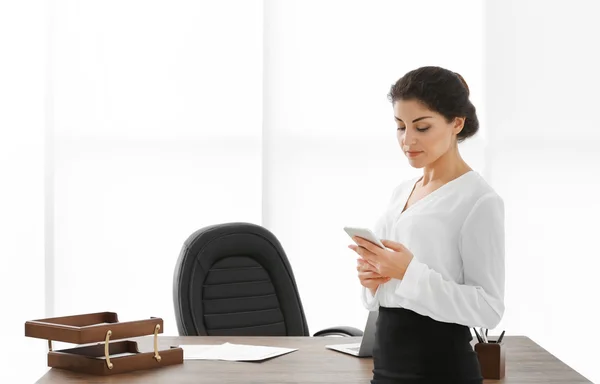 Succesvolle volwassen zakenvrouw met mobiele telefoon in haar kantoor — Stockfoto