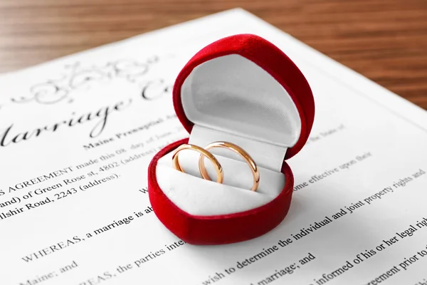 Caixa vermelha aberta com anéis de casamento dourados no contrato de casamento, close-up — Fotografia de Stock