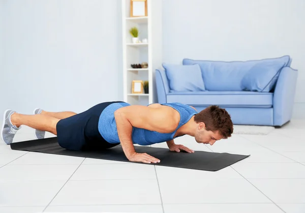Jovem fazendo exercícios no tapete no quarto — Fotografia de Stock