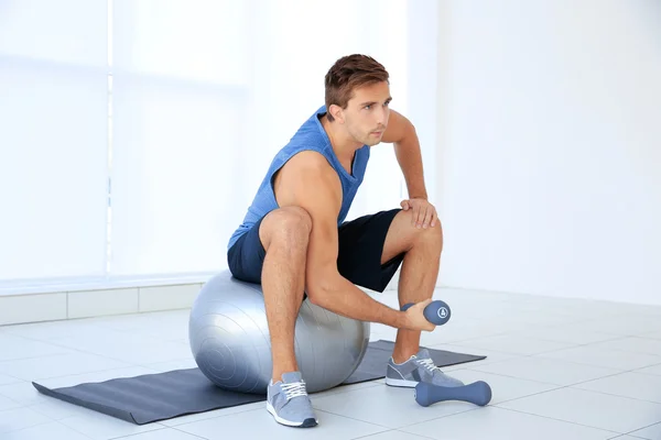 Young man doing exercises with dumb-bells and ball on rug — Stock Photo, Image