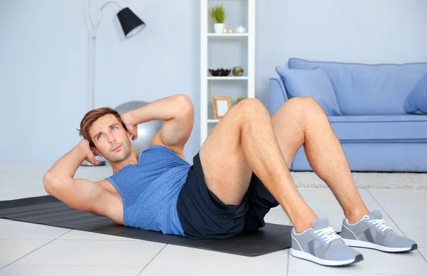 Young man doing exercises on rug in room — Stock Photo, Image