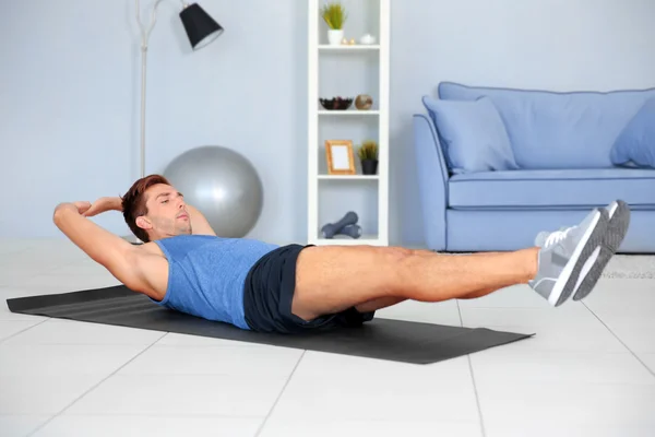 Jovem fazendo exercícios no tapete no quarto — Fotografia de Stock