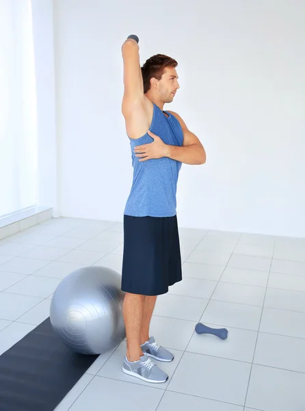 Junger Mann macht Übungen mit Glöckchen und Ball auf Teppich — Stockfoto