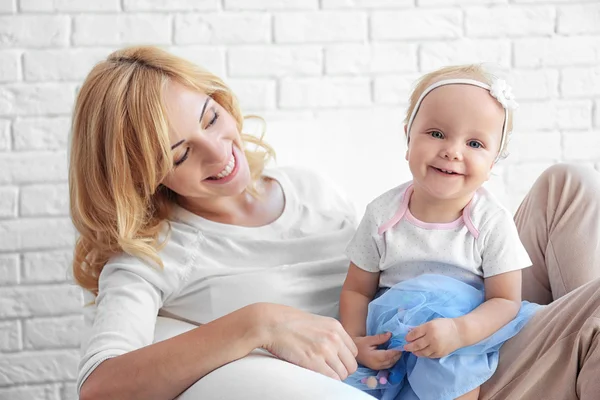 Mor med dotter sitter i fåtölj på vitt tegel vägg bakgrund — Stockfoto