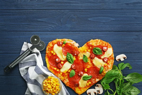 Pizza saborosa em forma de coração e seus ingredientes em fundo de madeira — Fotografia de Stock