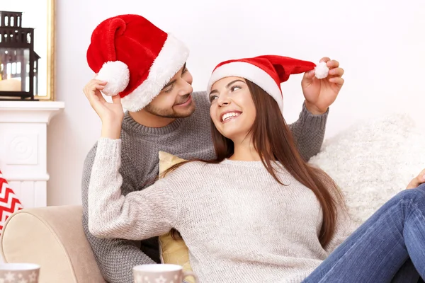 Casal jovem em chapéus de Papai Noel descansando em casa — Fotografia de Stock