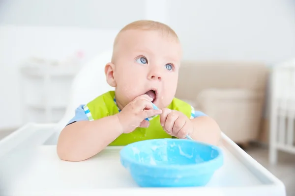 Little baby eating from bowl with spoon indoors Stock Picture