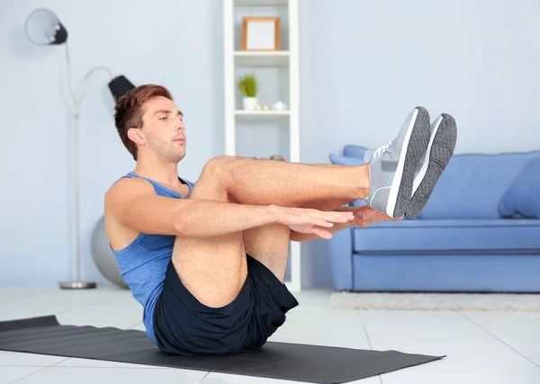 Young man doing exercises on rug in room Royalty Free Stock Photos