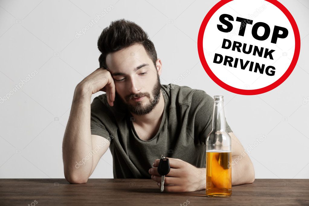 Drunk young man with car key and beer bottle at bar. Sign with text STOP DRUNK DRIVING on background.