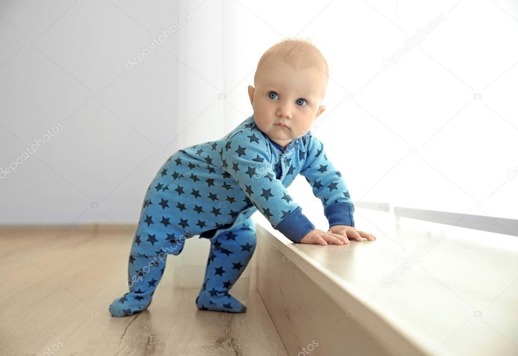 Adorable little baby standing beside wooden windowsill