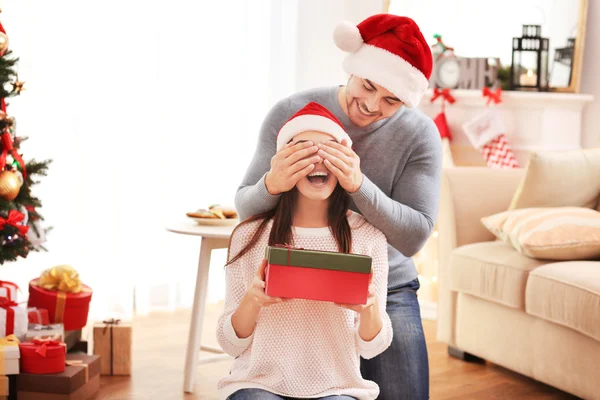 Uomo sorprendente la sua ragazza con scatola regalo di Natale al chiuso — Foto Stock