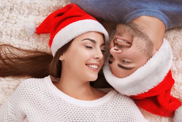 Giovane coppia a Babbo Natale cappelli sdraiato su tappeto di pelliccia in casa — Foto Stock