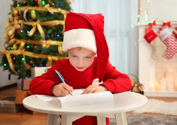 Χαριτωμένο μικρό αγόρι γράφει γράμμα στον Άγιο Βασίλη στο τραπέζι — Φωτογραφία Αρχείου