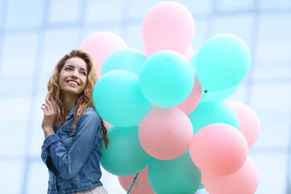 Hermosa mujer joven con globos de colores sobre fondo borroso — Foto de Stock