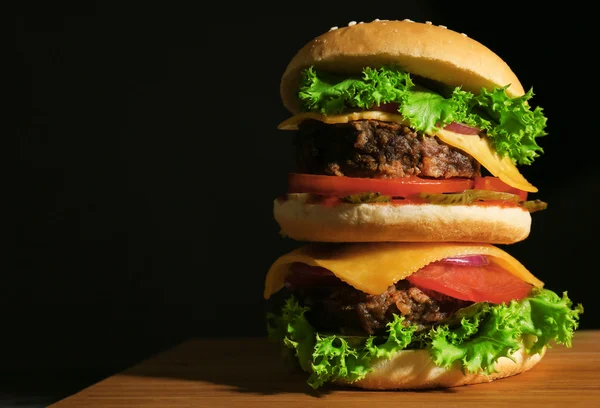 Leckere Burger auf Holzbrett auf schwarzem Hintergrund — Stockfoto