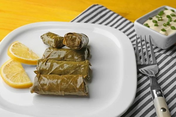 Um prato de Dolma recheado delicioso com molho e limão no fundo de madeira amarelo — Fotografia de Stock