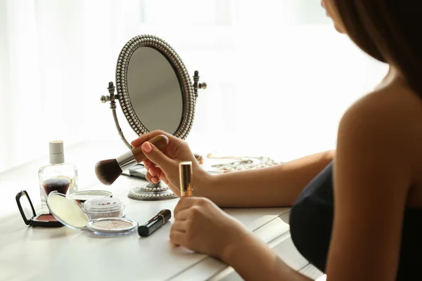 Beautiful young woman looking in mirror while applying makeup