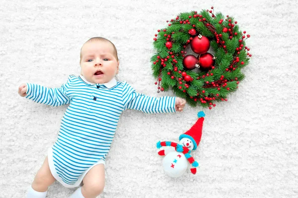 Niedliches Baby und Weihnachtskranz auf weißer Bettdecke liegend — Stockfoto