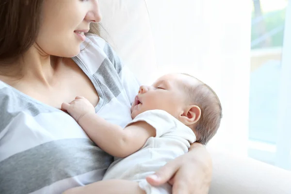 Porträtt av ganska ung kvinna anläggning sovande baby på ljus bakgrund — Stockfoto