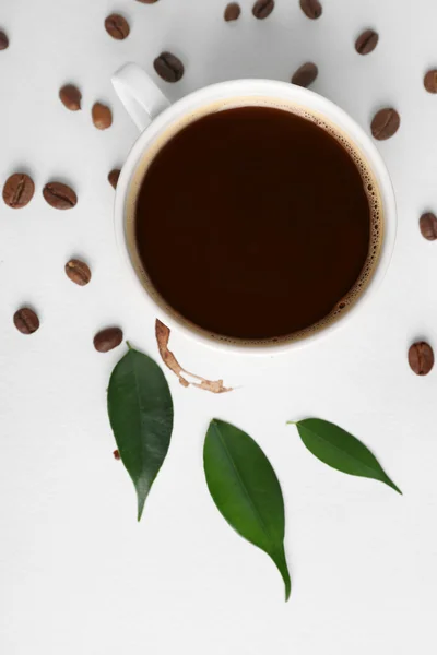 Xícara de café com grãos, folhas verdes e mancha no fundo branco, close-up — Fotografia de Stock