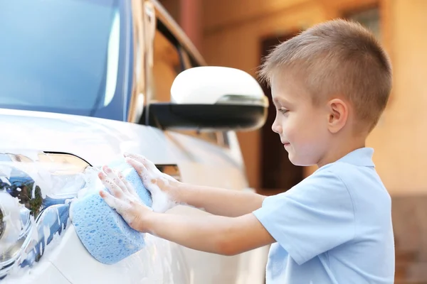 Маленький мальчик моет машину с губкой на улице — стоковое фото