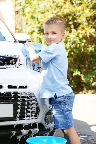 Liten pojke tvätta bilen med svamp på gatan — Stockfoto