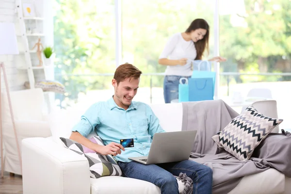 Jonge man met laptop online winkelen en vrouw op achtergrond — Stockfoto