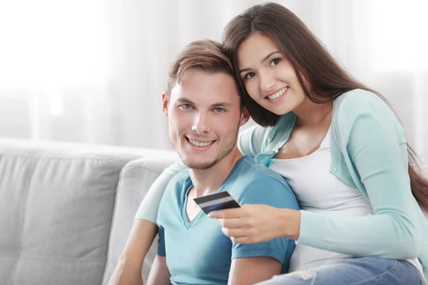 Happy couple with credit card sitting on sofa at home — Stock Photo, Image