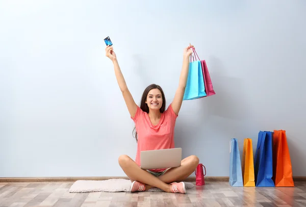 Boldog fiatal nő színes bevásárló táskák és ülő földre laptop — Stock Fotó