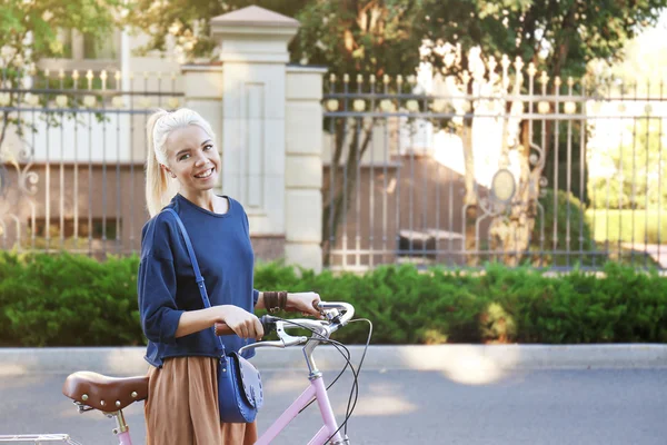 Mujer joven y bonita con bicicleta en el parque sobre fondo borroso — Foto de Stock