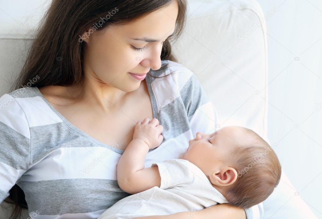 Portrait of pretty young woman holding sleeping baby on light background