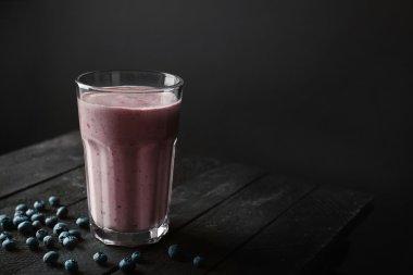 Lezzetli güler yüzlü ve koyu arka plan karşı ahşap masa üzerinde yaban mersini ile cam