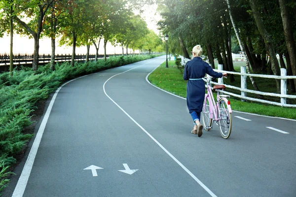 Mujer joven con bicicleta caminando a lo largo de la bicicleta en el parque verde — Foto de Stock