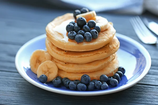 Plate med velsmakende pannekaker, bananskiver og bær på trebord, tett utsyn – stockfoto