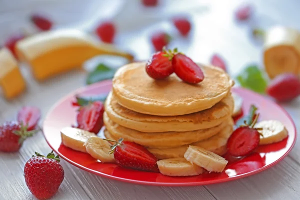 Teller mit leckeren Pfannkuchen, Bananenscheiben und Erdbeeren auf Holztisch, Nahsicht — Stockfoto