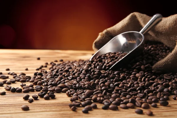Café en grains, sac et cuillère sur table en bois sur fond sombre, vue rapprochée — Photo