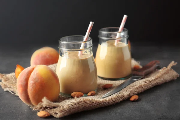 Vasetti di massone con frullato, pesche e tovagliolo sul tavolo grigio — Foto Stock