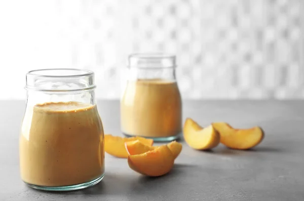 Mason jars with tasty smoothie and peach on table — Stock Photo, Image